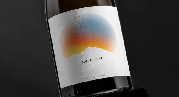 Primer plano de la etiqueta del vino Siguín 7:47 donde se lee "Vino de Madrid - 100% Garnacha", con un diseño artístico de un sol sobre una montaña.